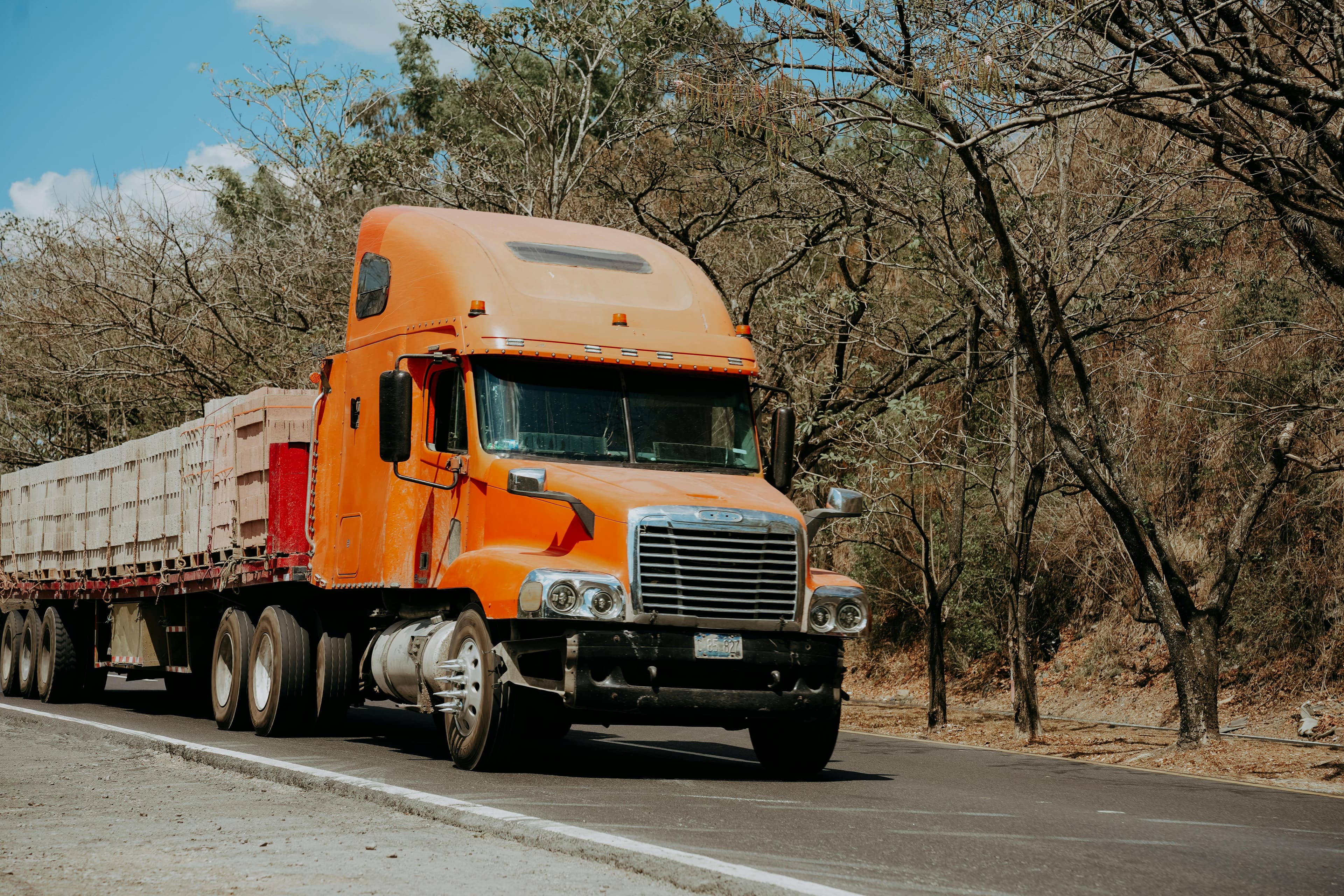 Orange semi-truck on a tree-lined road
