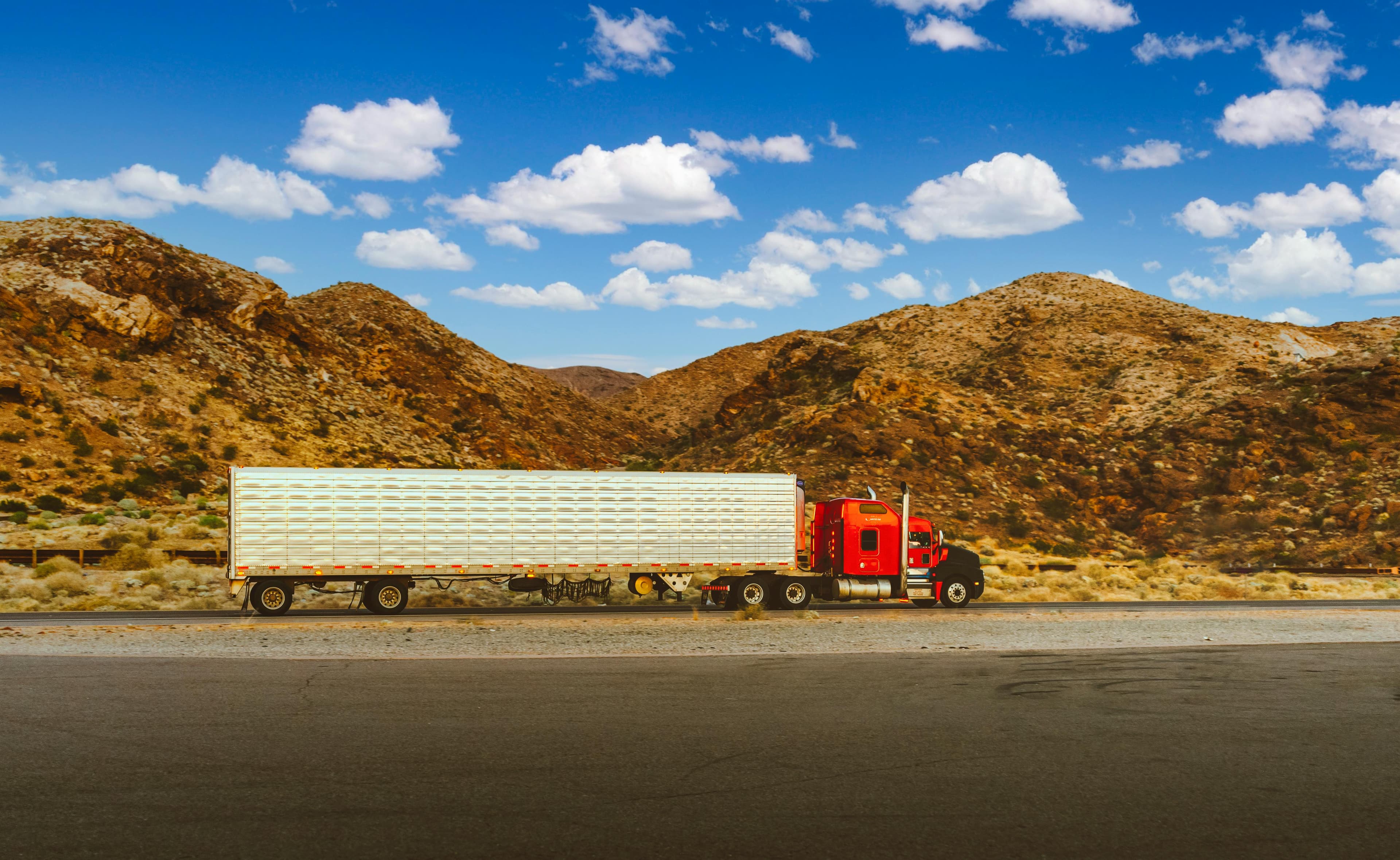 Red semi-truck with reefer trailer parked against a desert mountain backdrop