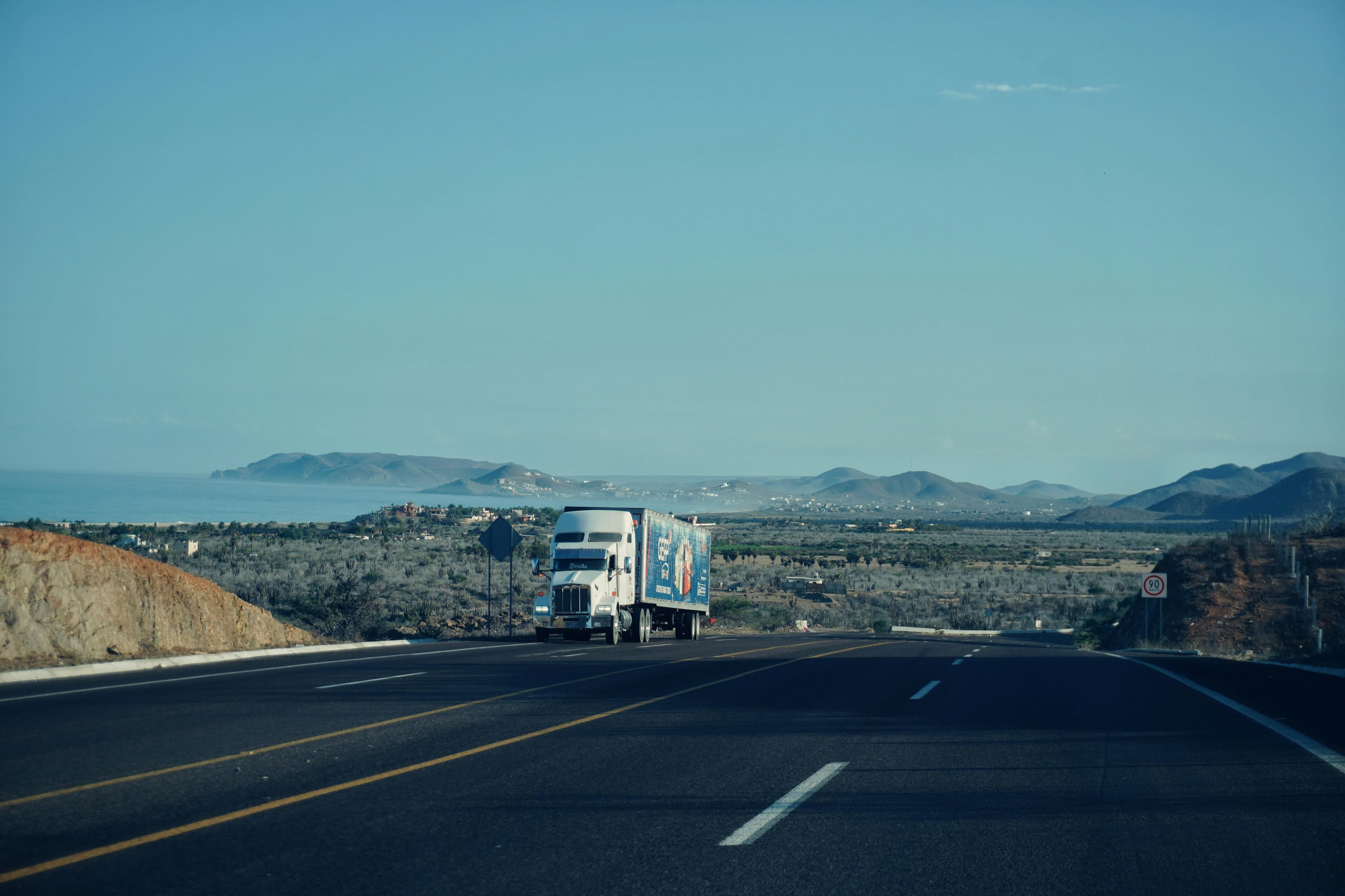 Semi-truck on a coastal highway with mountains and ocean in the distance