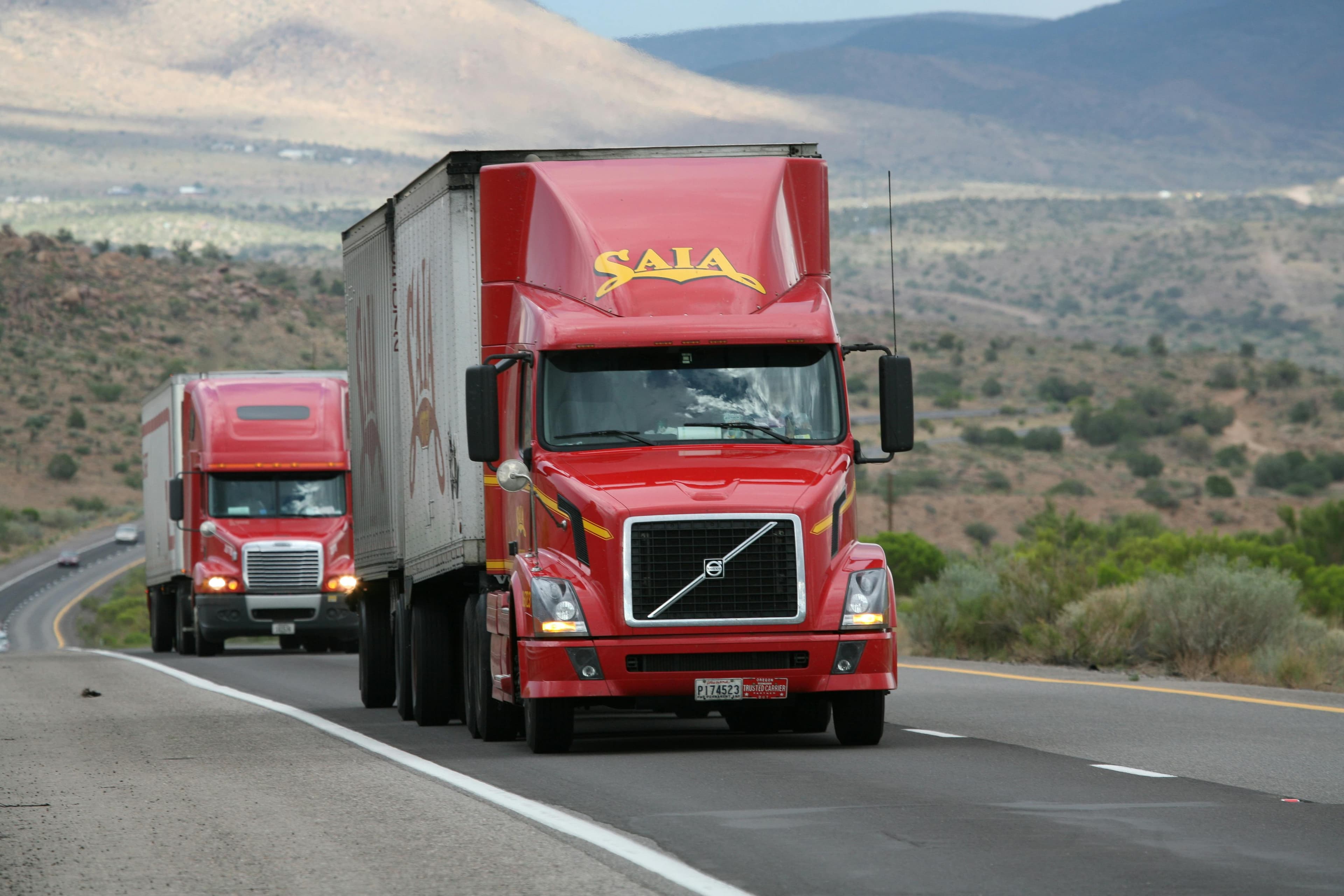 Two red semi-trucks driving down a desert highway